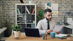 Stressed upset businessman looking at document waving head sighing thinking about problem