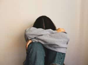 woman sitting on the floor wearing gray sweatshirt head hidden in her arms