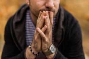 close up of man wearing black hoodie with hands together in front of his mouth