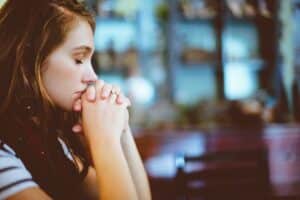 brunette woman with burgundy scarf hands folded in front of her contemplating how to cope with triggers in recovery from addiction